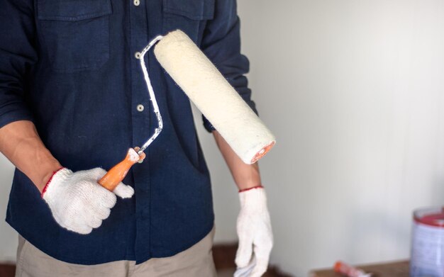 Midsection of man holding paint roller while standing against wall