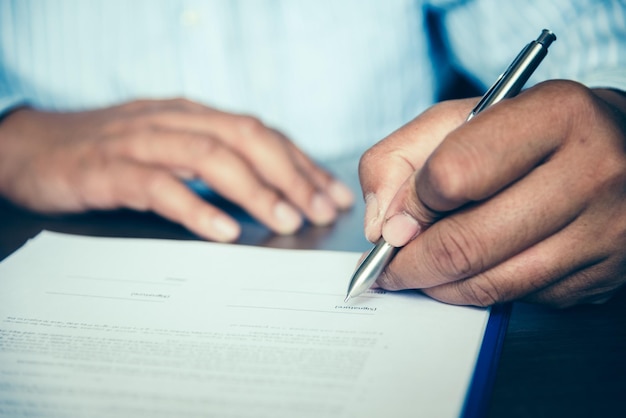 Photo midsection of man holding pen over paper on table