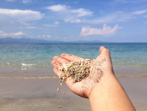 Midsection of man holding sand at beach against sky