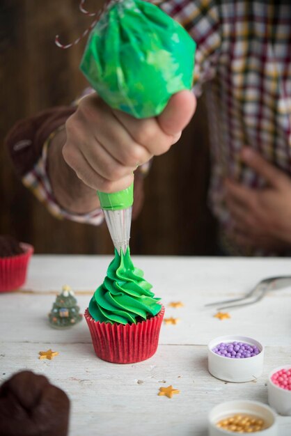 Foto sezione centrale dell'uomo che fa la glassa sul cupcake al tavolo