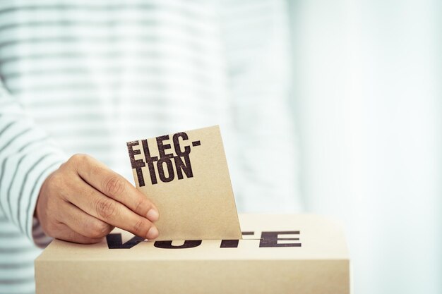 Photo midsection of man inserting envelope in ballot box