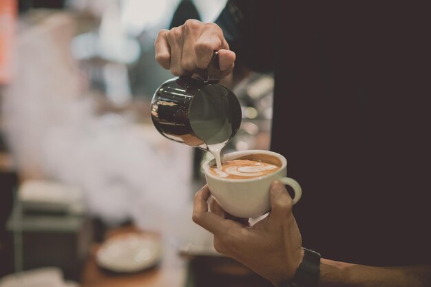 Foto sezione centrale di un uomo che versa latte nel caffè in un caffè