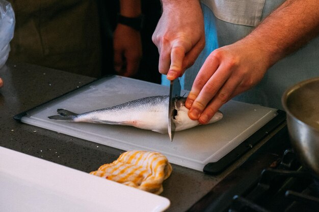 Foto sezione centrale di un uomo che prepara pesce fresco in una cucina su un tavolo da taglio