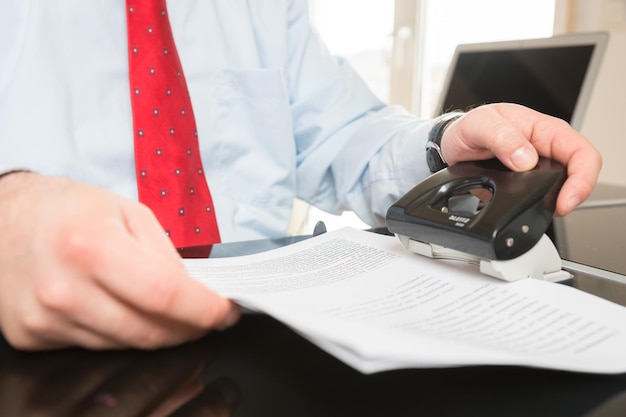 Midsection of man punching documents at desk in office