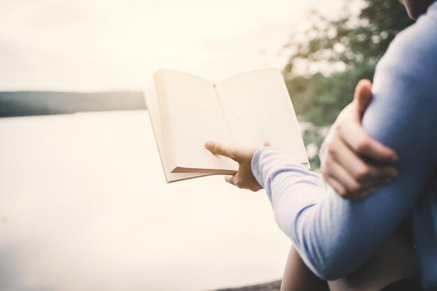 Foto sezione centrale di un uomo che legge un libro contro il cielo