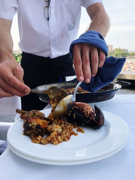 Midsection of man serving food in plate on table