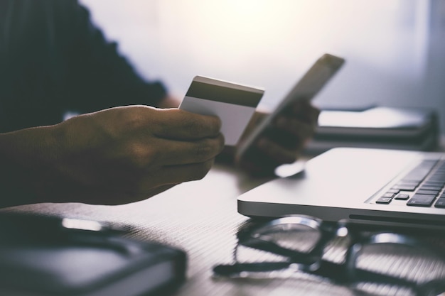 Midsection of man shopping online through mobile phone at table