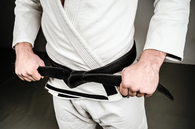 Photo midsection of man in sports uniform holding black belt over gray background