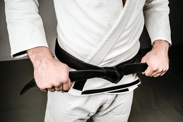 Photo midsection of man in sports uniform holding black belt over gray background