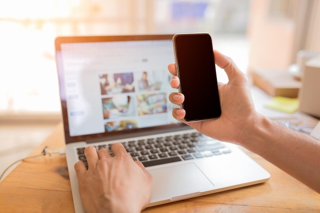 midsection of man using laptop while holding smartphone at home
