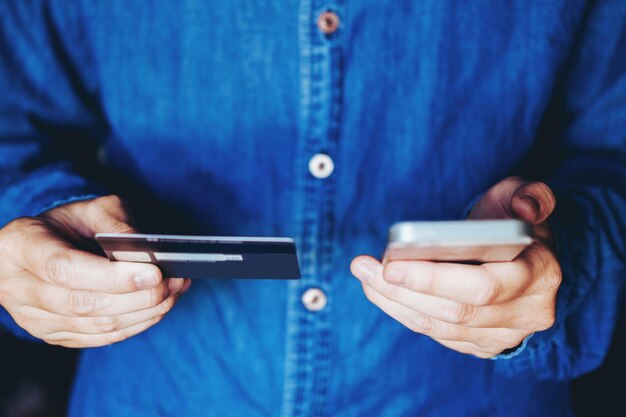 Foto sezione centrale di un uomo che usa il telefono cellulare mentre tiene in mano una carta di credito