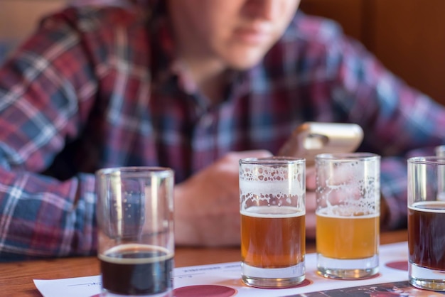 Foto sezione centrale di un uomo che usa il telefono mentre beve birra al tavolo