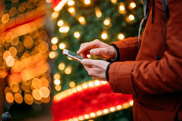 照らされたクリスマスツリーに対してスマートフォンを使用している人の中央部。