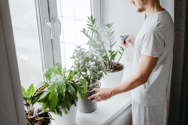 家で鉢の植物に水を注ぐ男の真ん中