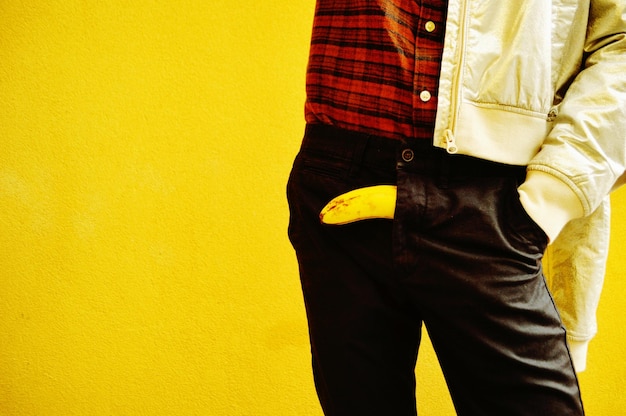 Midsection of man with banana standing against yellow background