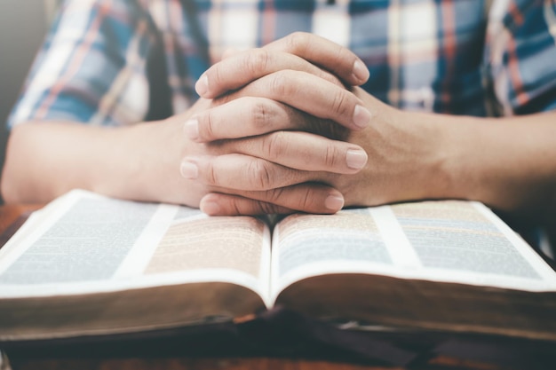 Photo midsection of man with hands clasped on open bible