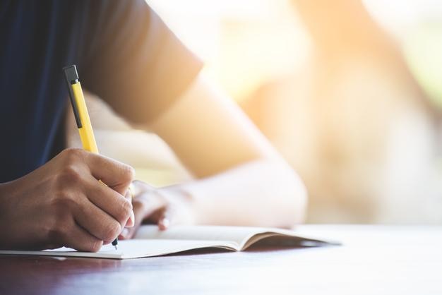 Midsection of man writing on book at table