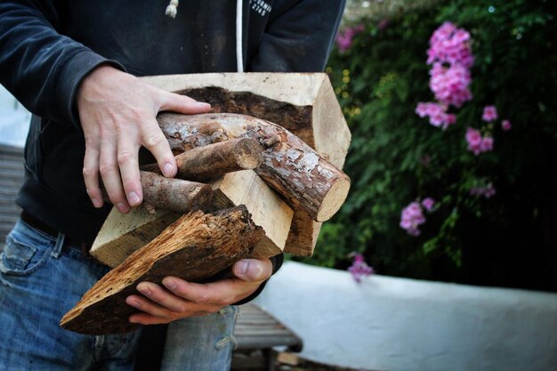 Midsection of mature man holding firewood while standing outdoors