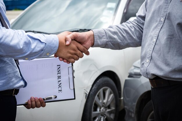 Photo midsection of men shaking hands with insurance paper by car