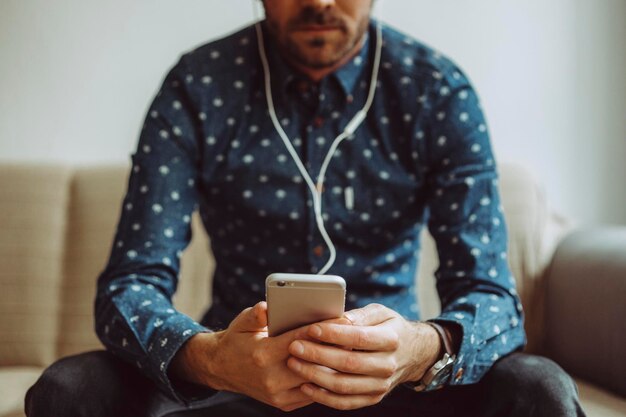 家のソファに座っている間に携帯電話を使っている中年男性のミッドセクション