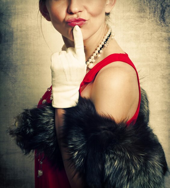 Photo midsection of mid adult woman in retro style clothing with finger on chin puckering lips against textured gray background