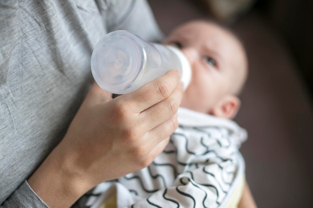 Midsection of mother feeding milk to baby boy with bottle at home