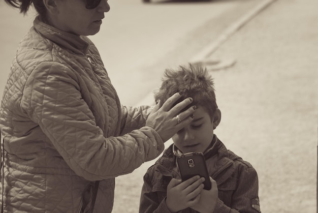 Photo midsection of mother standing by son using mobile phone