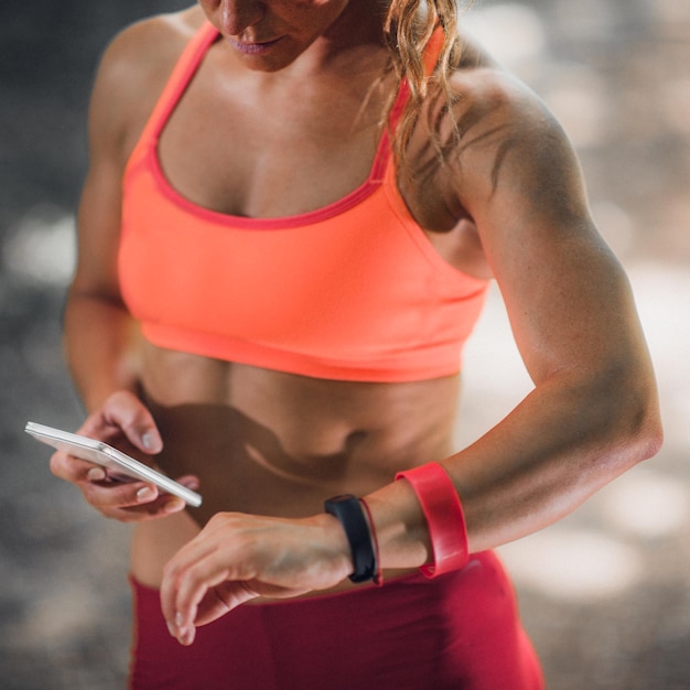 Foto sezione centrale di una donna muscolosa che indossa un fitness tracker mentre usa il telefono cellulare