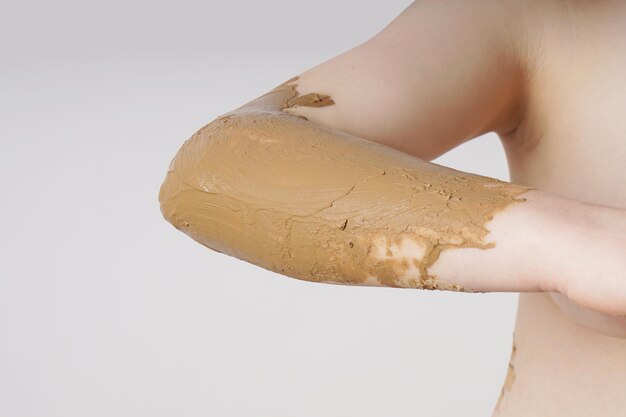 Foto sezione centrale di una donna nuda con il fango sul gomito contro uno sfondo bianco