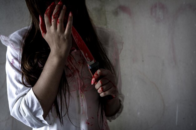 写真 壁に血で覆われたナイフを握っている邪悪な女性のミッドセクション