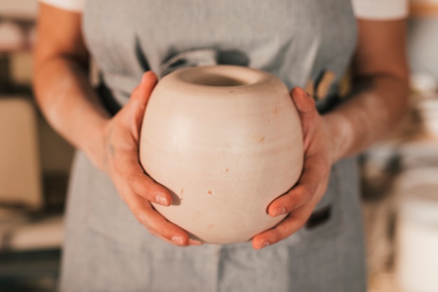 手作りの鍋を持っている女性の陶工の手の中央部