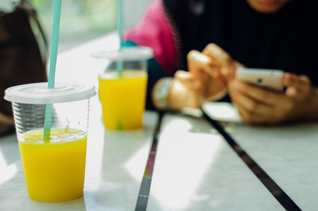 写真 レストランのテーブルでマンゴージュースで携帯電話を使っている女の子のミッドセクション