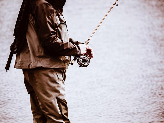 写真 湖の近くで釣り竿を握っている男の真ん中