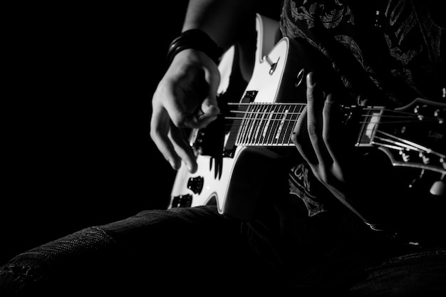 Фото Средняя часть человека, играющего на гитаре, сидящего на черном фоне