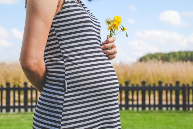 写真 空に向かって立っている間に花を握っている妊娠中の女性のミッドセクション