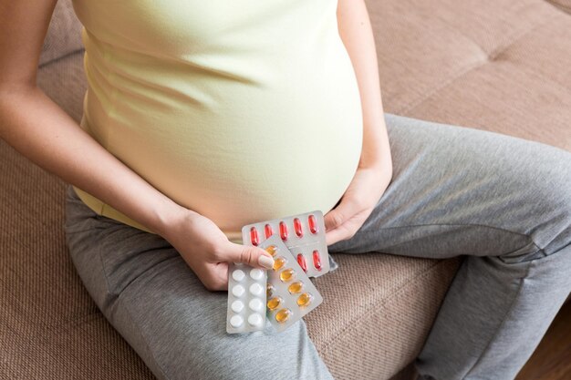 写真 家のソファでビタミン剤を飲んでいる妊婦のミッドセクション