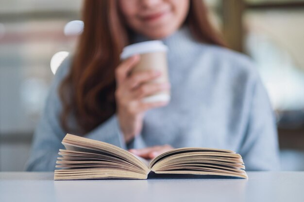 写真 テーブルの上で本を読みながらコーヒーカップを握っている女性のミッドセクション