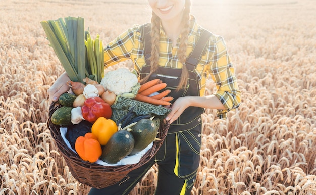 写真 植物のそばに立っている女性がバスケットに野菜をんでいます