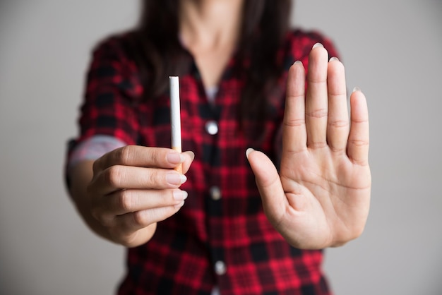 Фото Средняя часть женщины, показывающая жест остановки и держащая сигарету, стоя на сером фоне