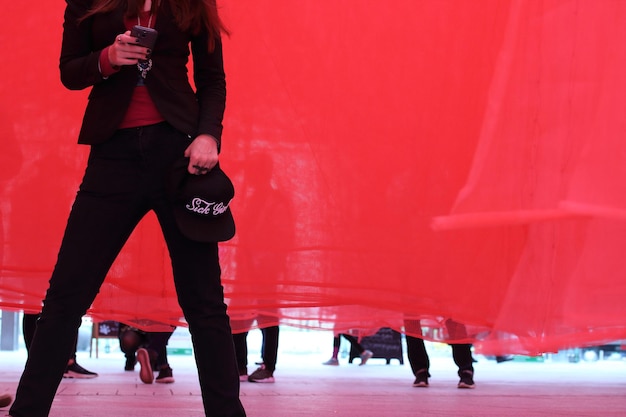 Фото Средняя часть женщины, использующей мобильный телефон, стоящей на красной занавеске