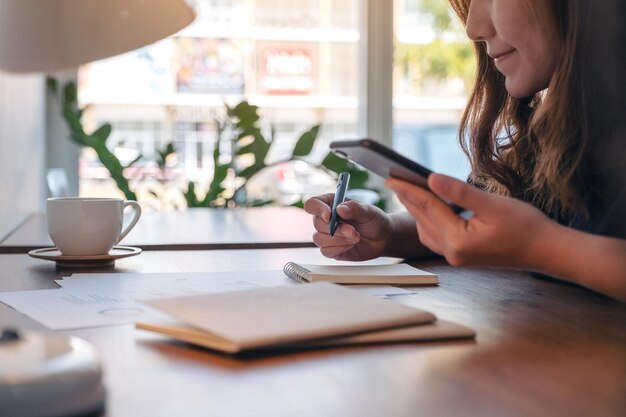 写真 カフェでノートパッドに書きながら携帯電話を使っている女性のミッドセクション