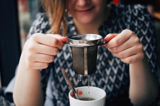 写真 レストランで紅茶カップの上にインフューザーを握っている若い女性のミッドセクション