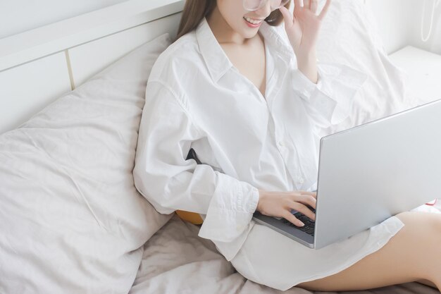 사진 집에서 침대에 앉아 노트북을 사용하는 젊은 여성의 중간 섹션