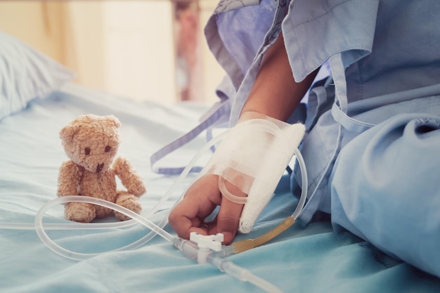 Midsection of patient sitting by teddy bear on hospital bed