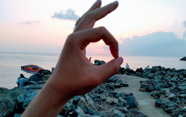 Foto sezione centrale della mano di una persona che fa un gesto contro il mare e il cielo