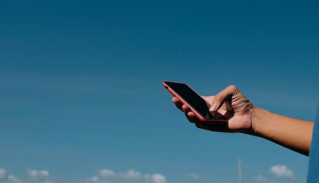 Foto sezione centrale di una persona che tiene un telefono cellulare contro il cielo blu
