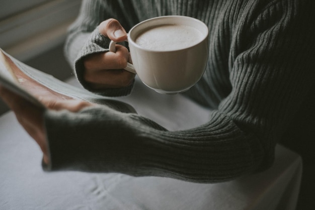 Photo midsection of person reading newspaper while holding coffee cup on table