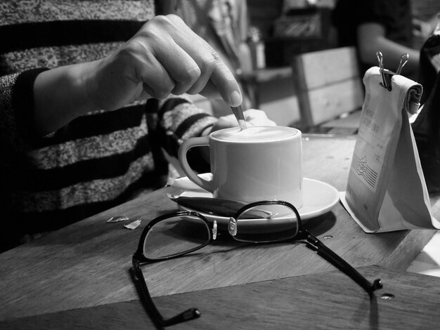 Foto sezione centrale di una persona che mescola il caffè con gli occhiali sul tavolo