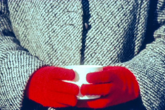 Средняя часть человека в теплой одежде, держащего чашку с кофе