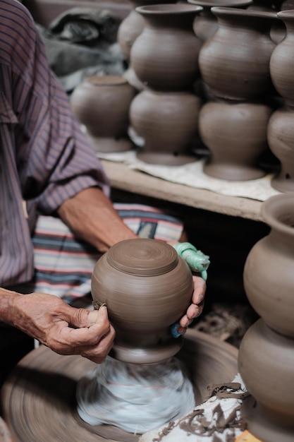 midsection of potter shaping earthenware on pottery wheel at workshop